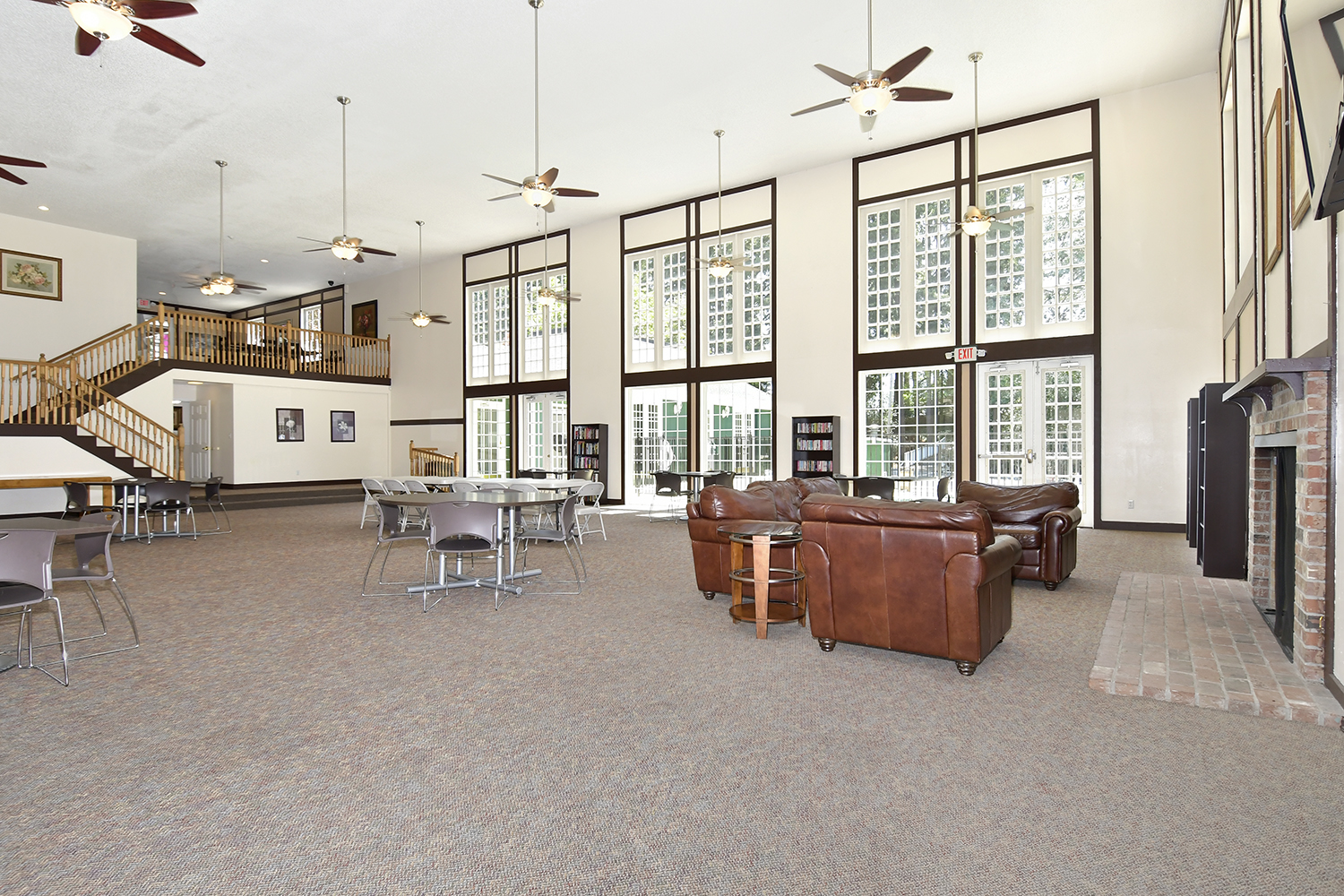 Large community room with tall ceiling and floor to ceiling windows. Tables and chairs to lounge in. Stairs to the second level.