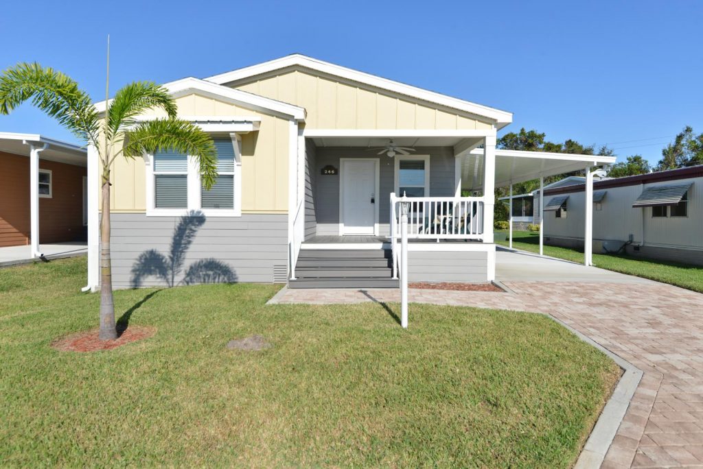 Beautiful new home with two tone colors of cream and light gray. Small covered front porch with ceiling fan. Four small steps take you from the porch to the walk way and driveway. Attached carport. Small palm tree growing in the front yard.