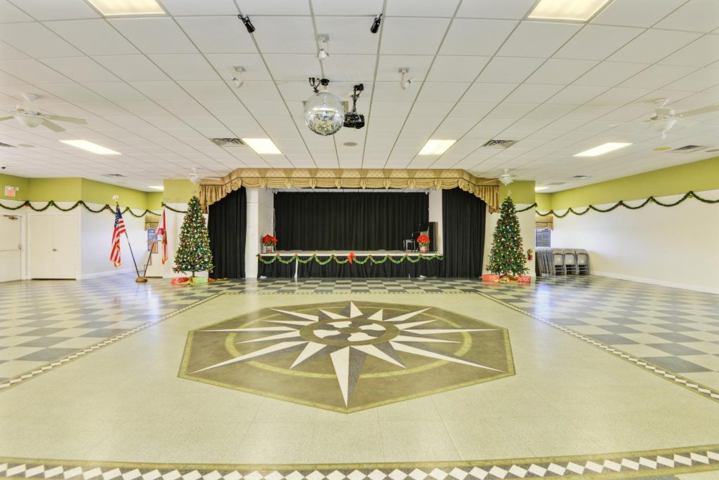 Large, spacious clubhouse that host many community wide events. A disco ball hands in the middle of the floor and 2 decorated Christmas trees sit at each side of the stage.