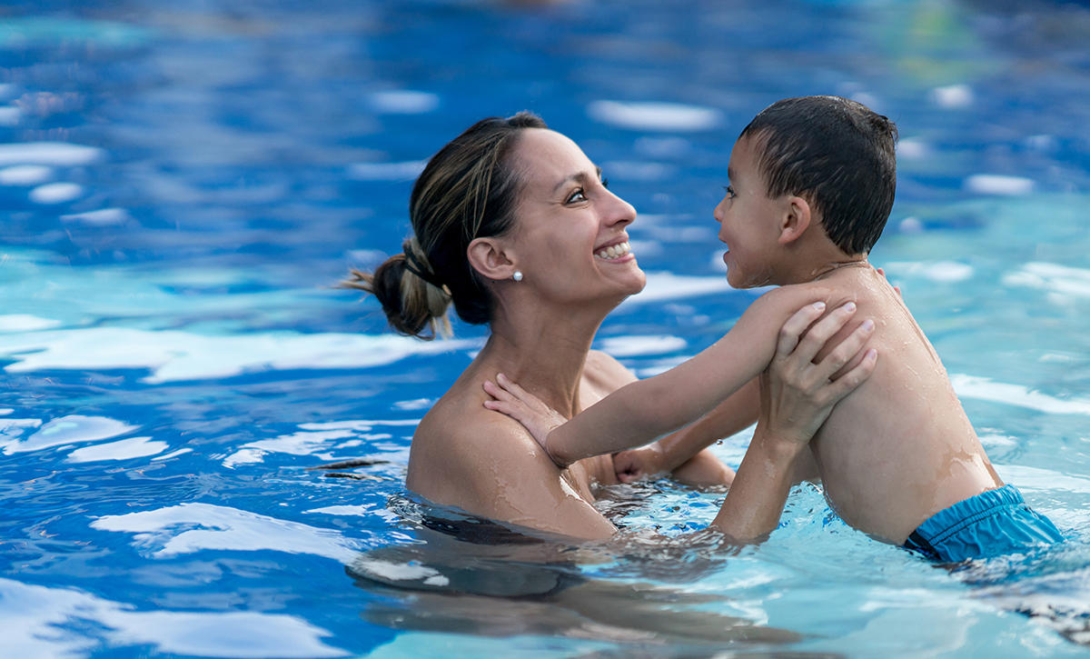 Beautiful young mom holding with excitement her son and holding him in the pool both smiling.