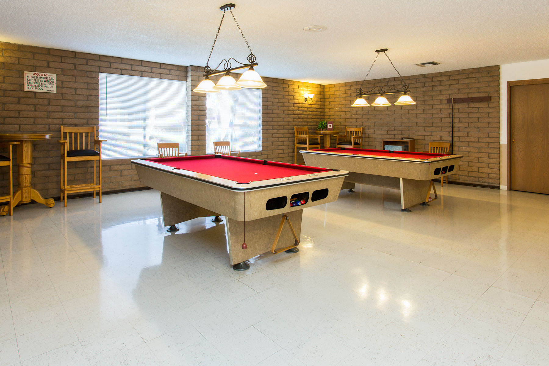 Billiards room equipped with two pool tables and seating areas. Walls lined with light brick to give a rustic feel.
