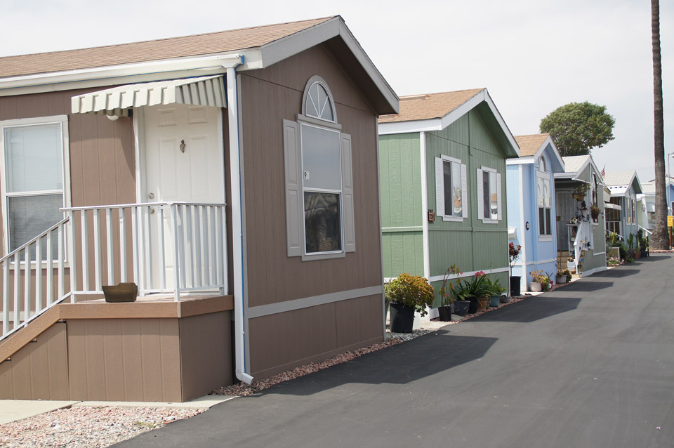 Tan, jade, and baby blue neighboring manufactured homes have a clean exterior and well-maintained landscape. The neutral colors give the community a warm feel.