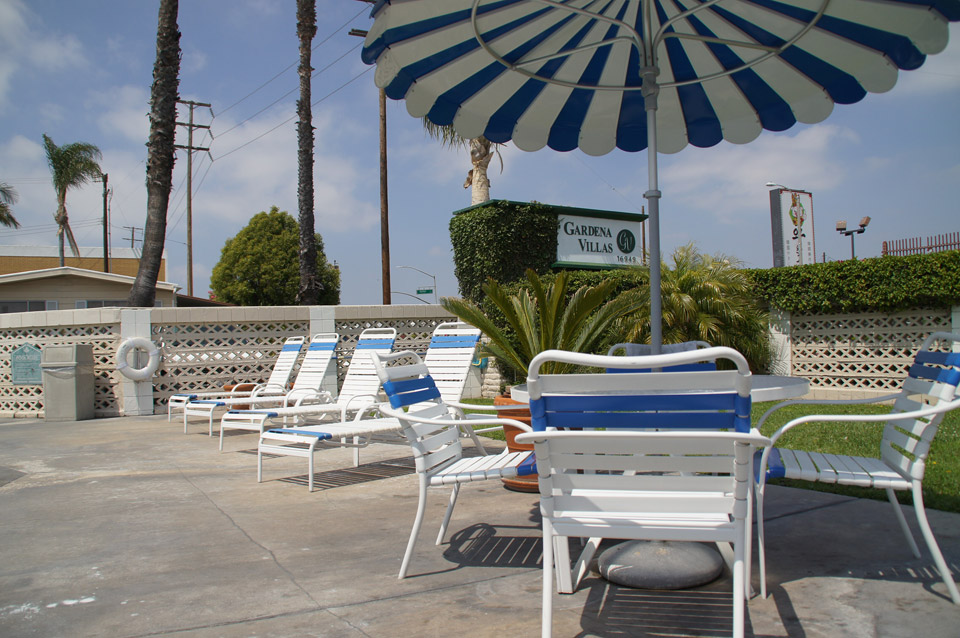 Outdoor lounge chairs for relaxation near the pool. Table with connected white and blue striped umbrella and chairs available for extra seating under the shade.