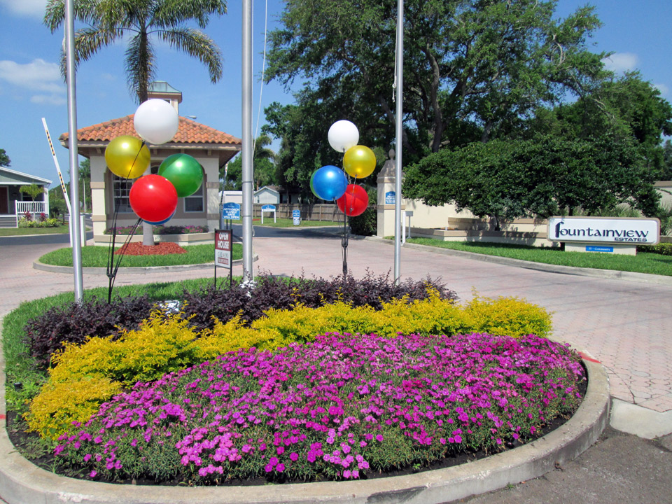 Purple and yellow flowers at front entrance with two balloon clusters of white, gold, green, red and blue balloons.
