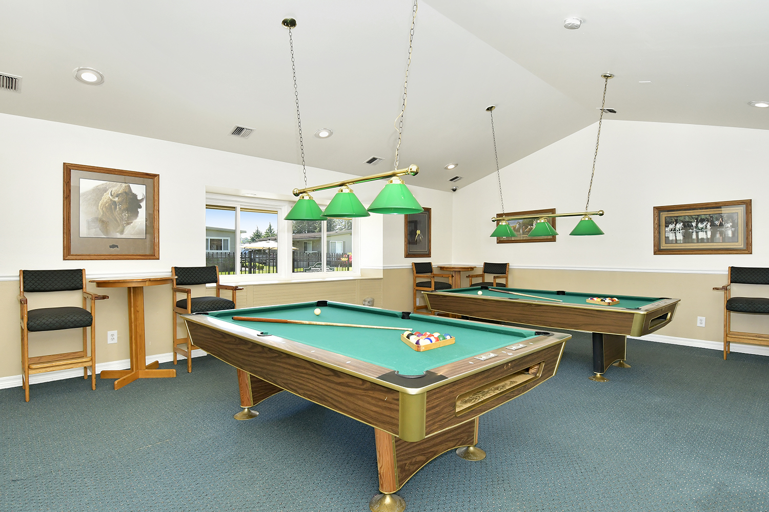Two billiard tables within the clubhouse for residents to enjoy. Surrounded by seating and small raised tables.