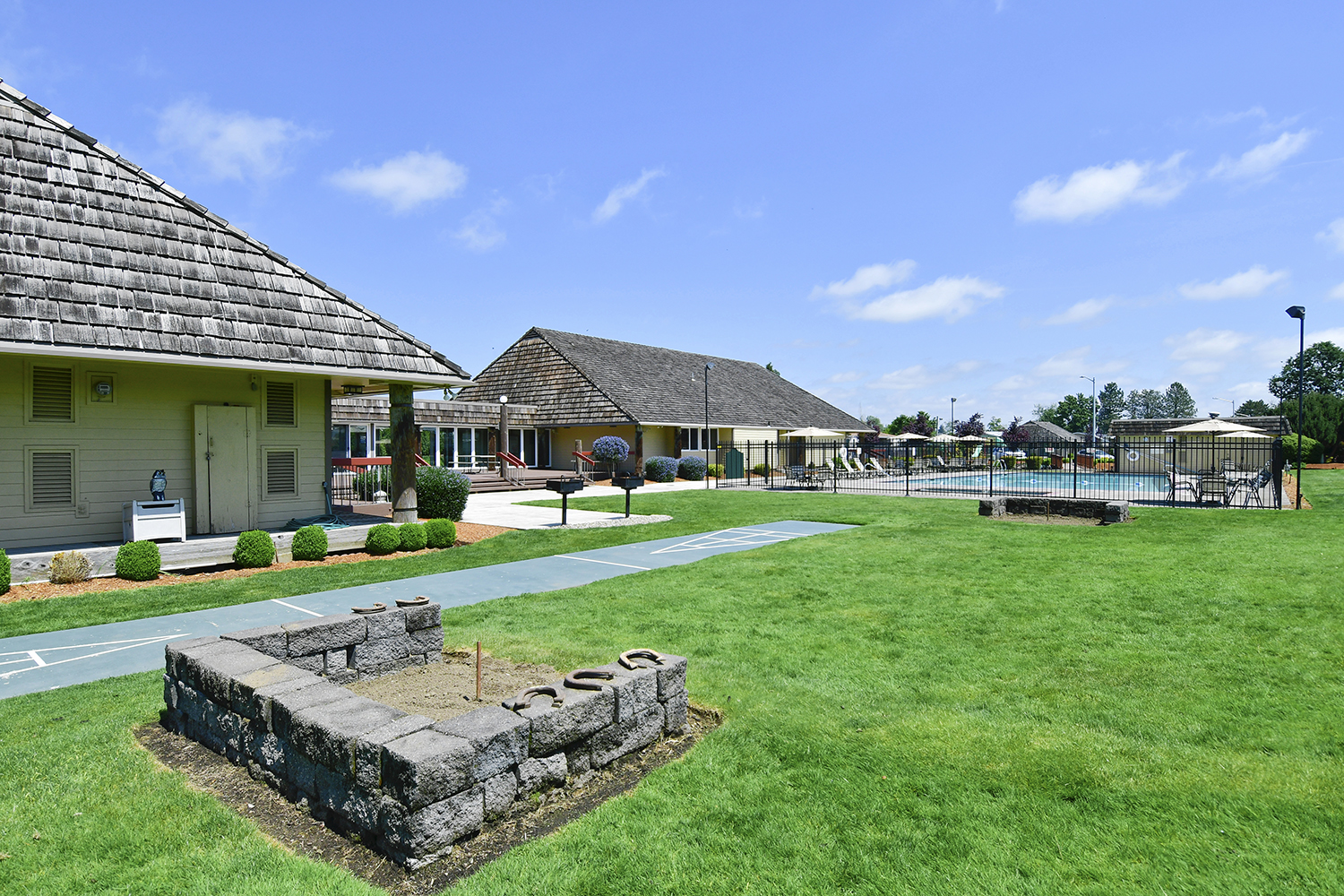 View of the horseshoe pit planted on beautiful green grass, neighboring the clubhouse, office and community pool.