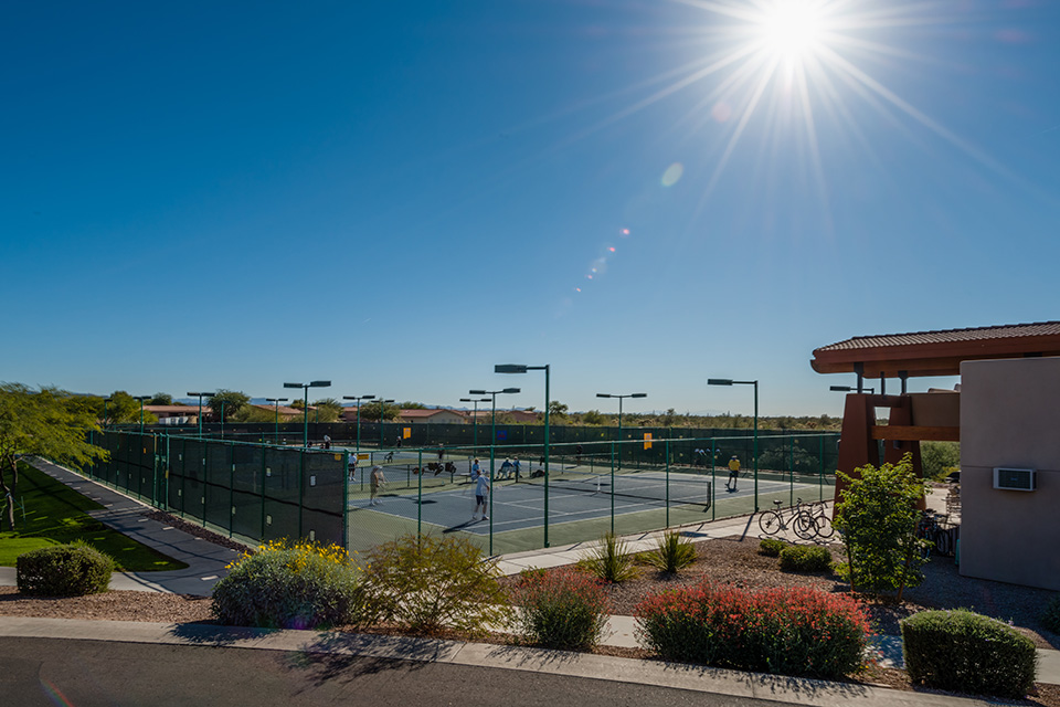 A sunny, cloudless day. People play pickleball at the pickleball courts.