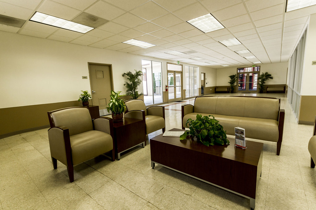Community center connected to the leasing office with light cream walls and brown bordering. Comfortable seating area for residents to enjoy with a dark wood coffee table surrounded by two individual sofas with a side table and one love seat.