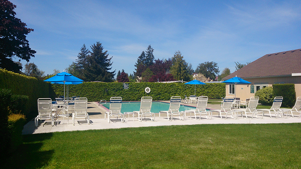 Swimming pool with lounge chairs, tables and blue umbrellas set up.