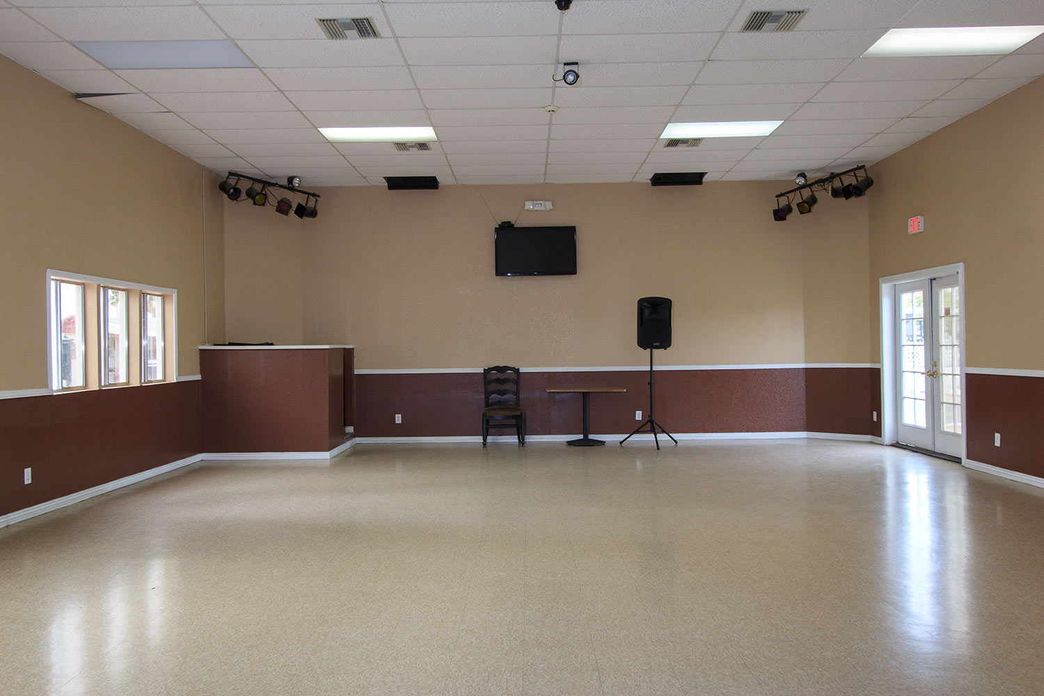 An open floor set up for dances with lights hung from ceiling, loud speaker and flat screen TV mounted to wall