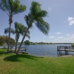 Green grass and palm trees lead up to the lake waters. Calm waters lap up to the docks.