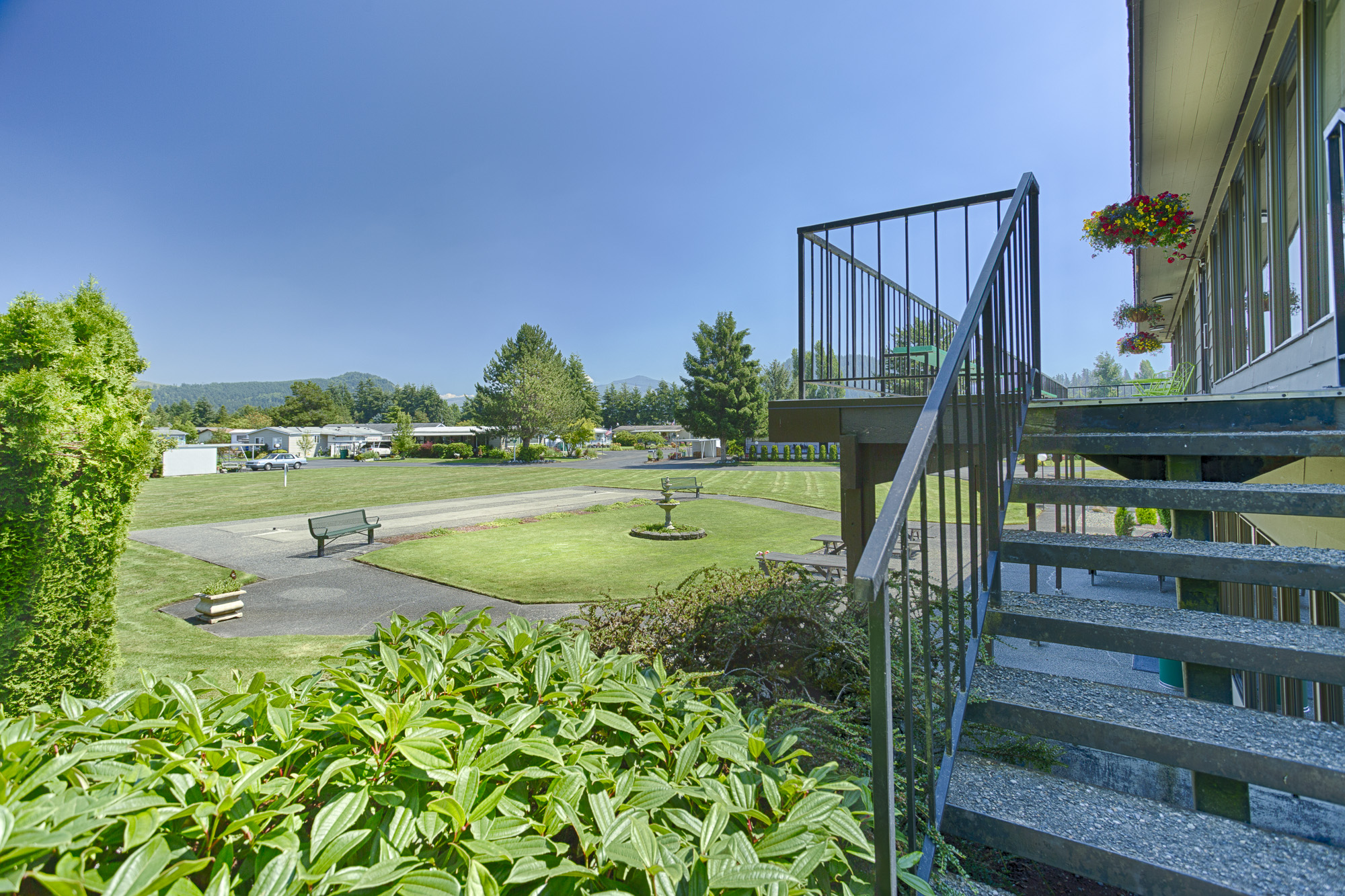 Open outdoor area with clean, cut grass, and well maintained landscape. Staircase leading up to the second level balcony of the community center.