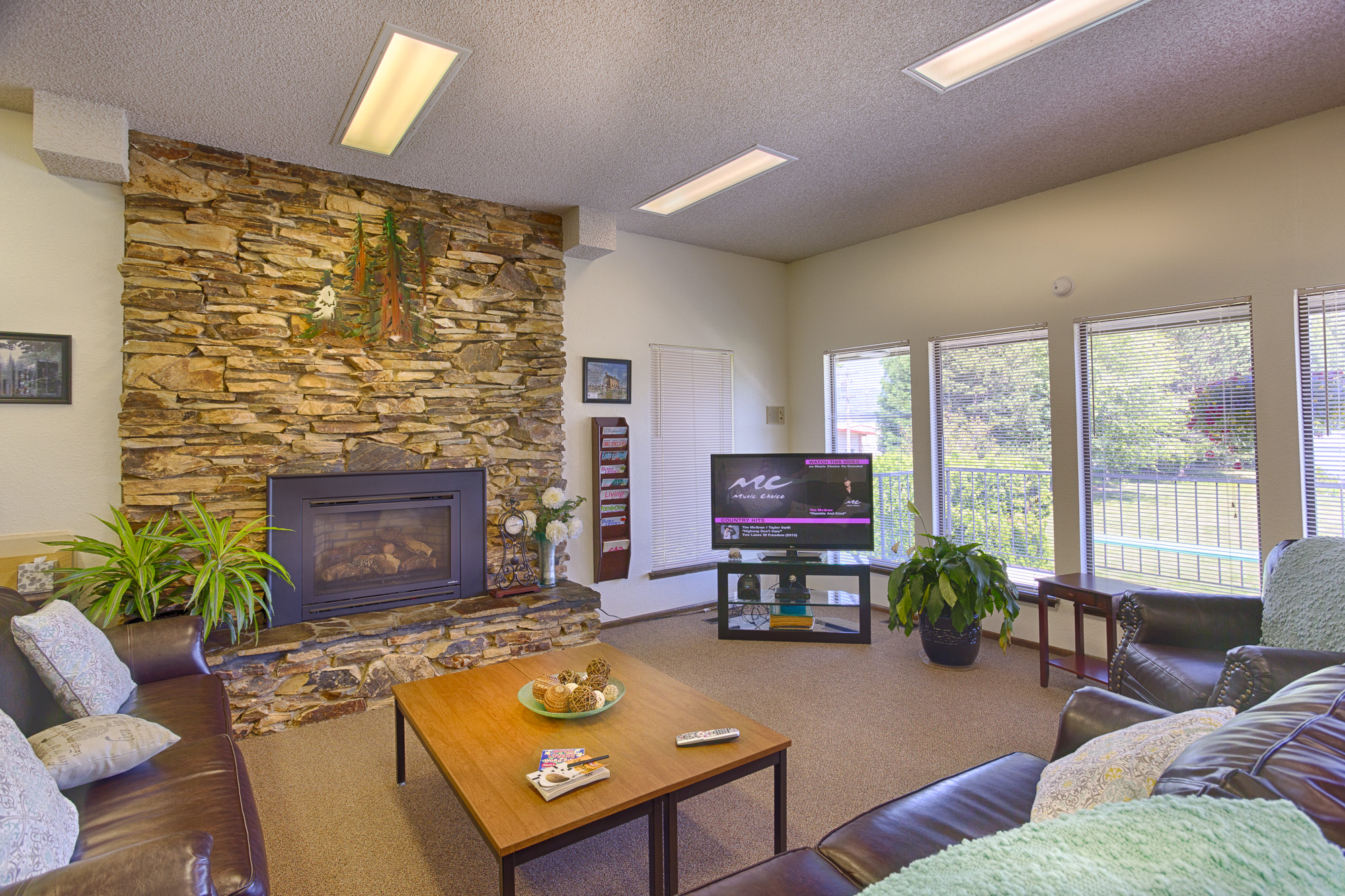 Tranquil community center with stone fireplace and flat screen television. Surrounded by brown leather couches for relaxation.